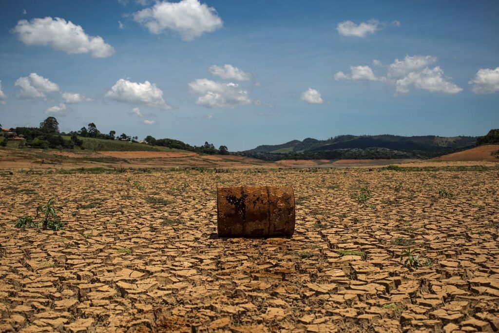 Objeto no centro da imagem em meio a um solo seco causado pelas mudanças climáticas, com árvores verdes no fundo